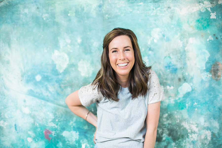 marketing coach, woman brand headshot laughing in front of a teal blue green abstract wallpapered wall