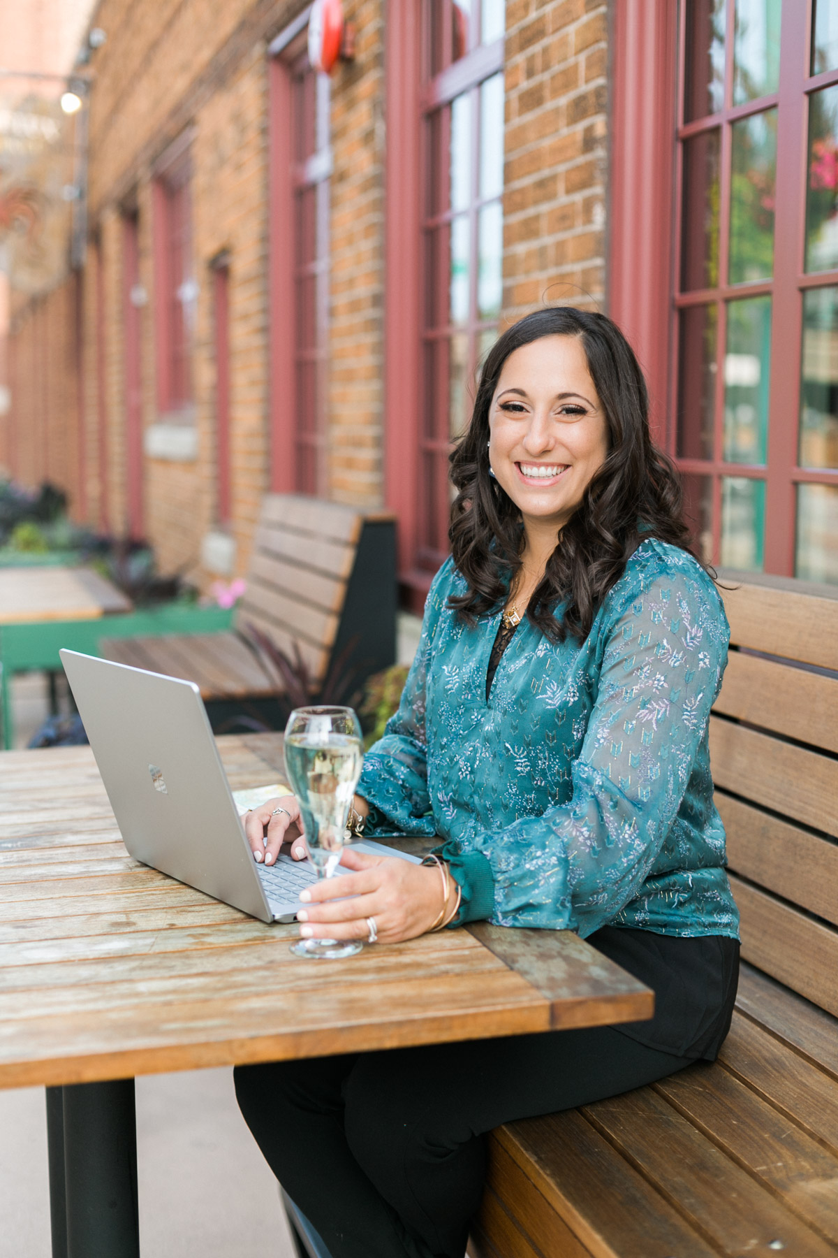 woman working on a laptop at patio restaurant with champagne, luxury travel designer, woman owned business, milwaukee wisconsin, photo by mybrandphotographer
