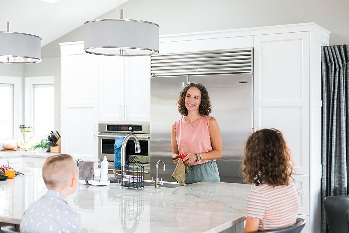 woman at kitchen sink looking at kids and washing vegetables