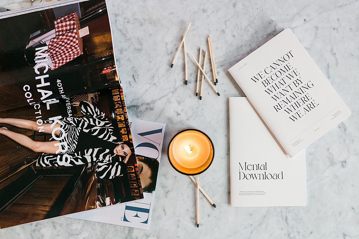 flatlay of business notebooks, candle and matches, and fashion magazine like Vogue
