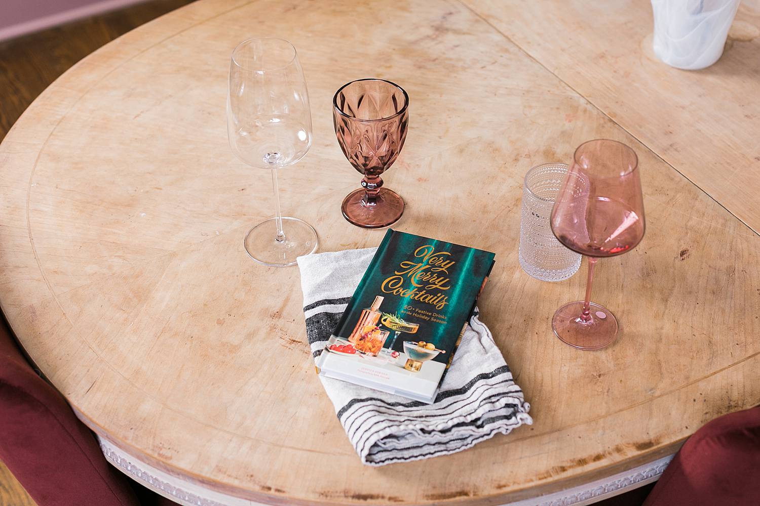 holiday cocktail recipe book and rose colored wine glasses on a dining room table