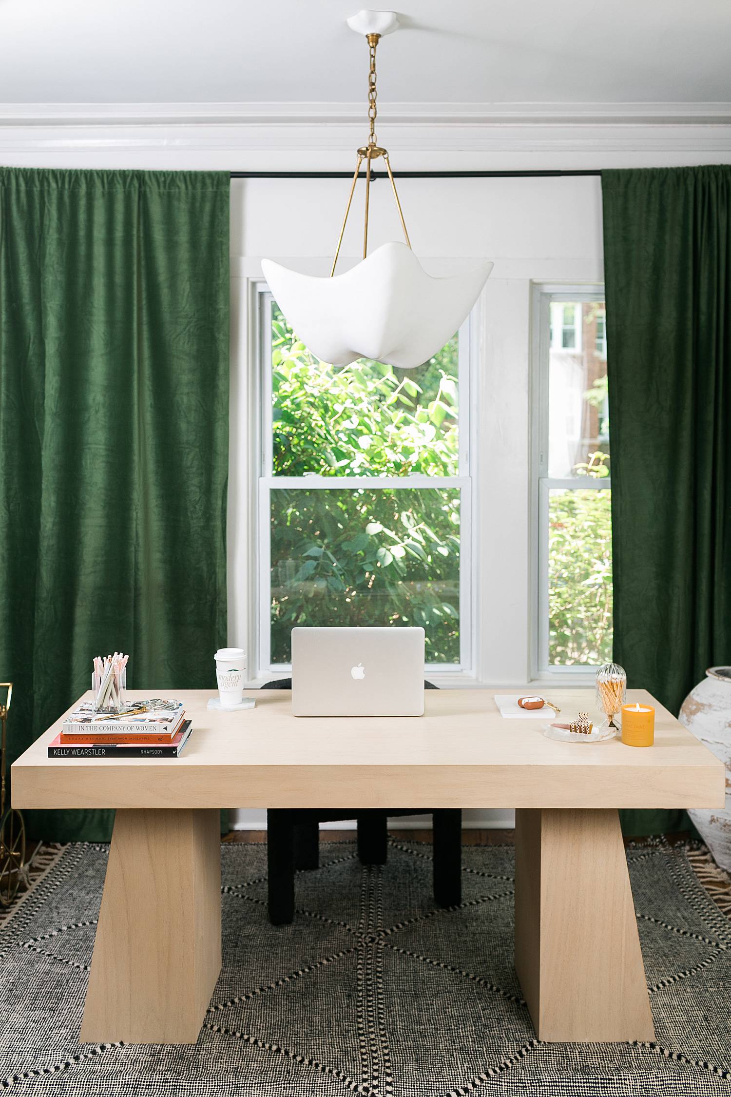 modern home office with light wooden desk and green curtains, macbook laptop on the desk and candle burning