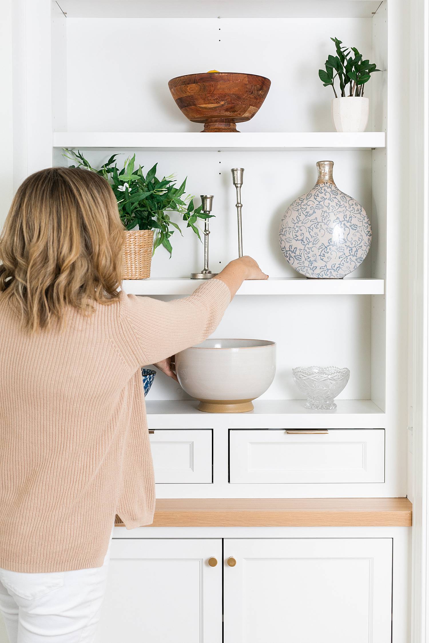 woman realtor arranging living room shelf, styling items on a shelf