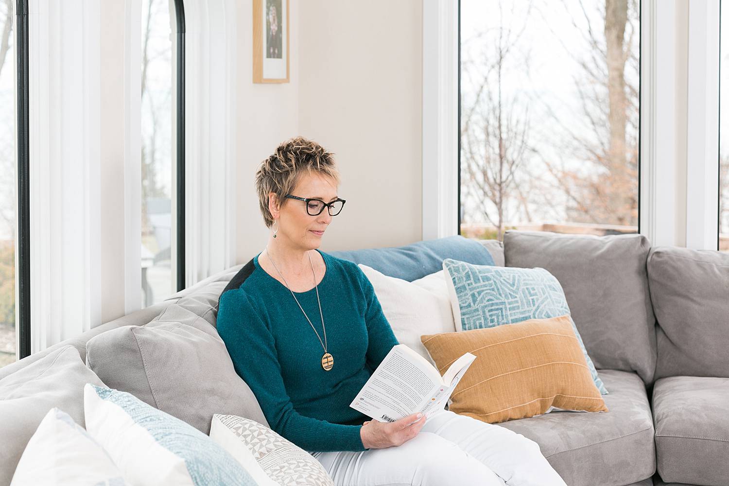 woman reading professional development book on living room couch