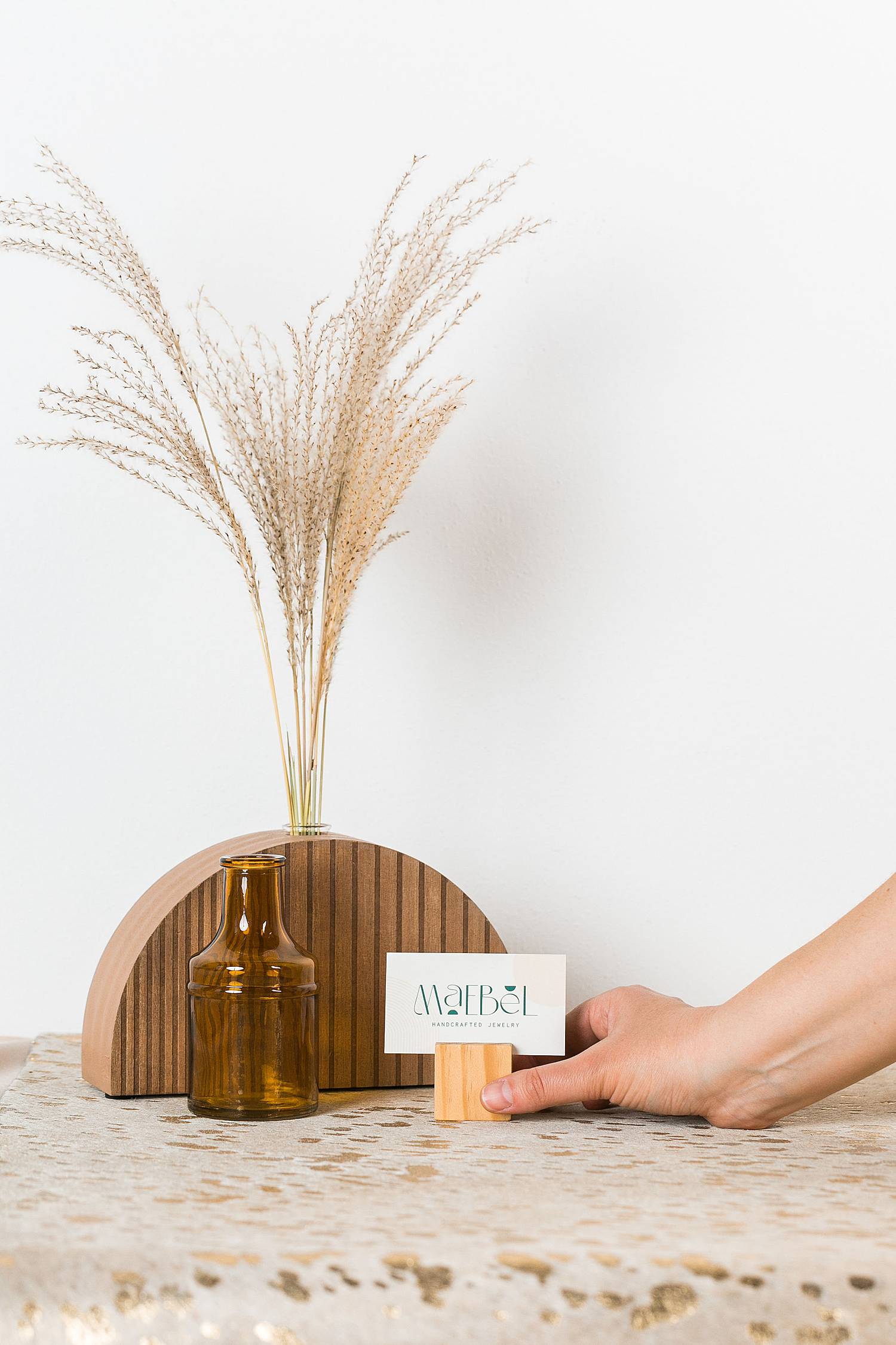 woman's hand holding business card in front of wooden vase and dried decorative grasses