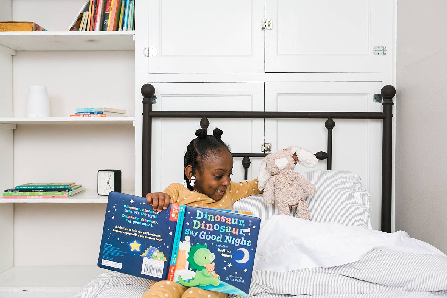 child reading book at bedtime with stuffed animal tucked into bed