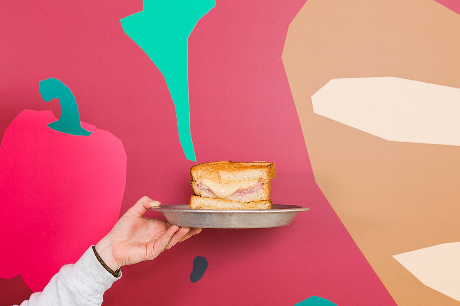 hand holding a sully's sandwich melt in front of red wall with food graphics