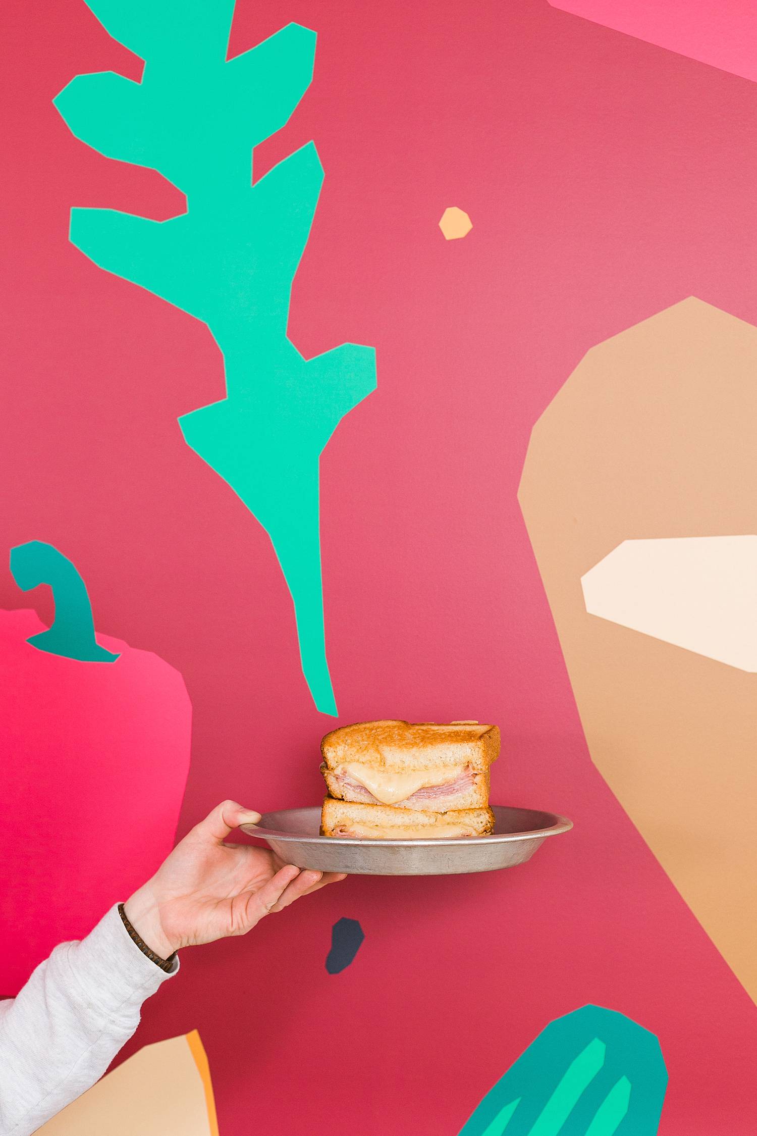 hand holding a sully's sandwich melt in front of red wall with food graphics