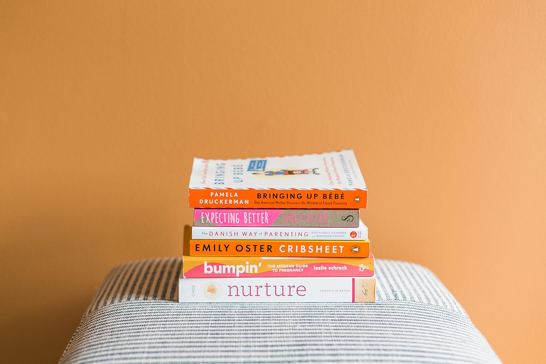 stack of modern birthing pregnancy and parenting books on striped ottoman and orange wall