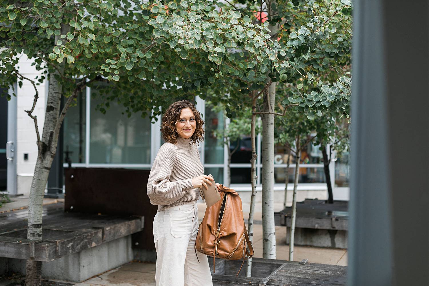 woman packing a brown leather bag and wearing a tan sweater and white pants