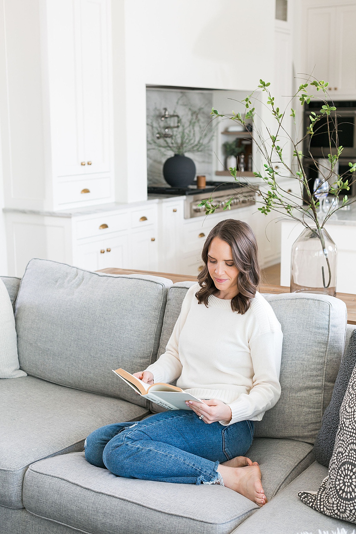 woman reading on couch wearing neutral sweater and denim jeans