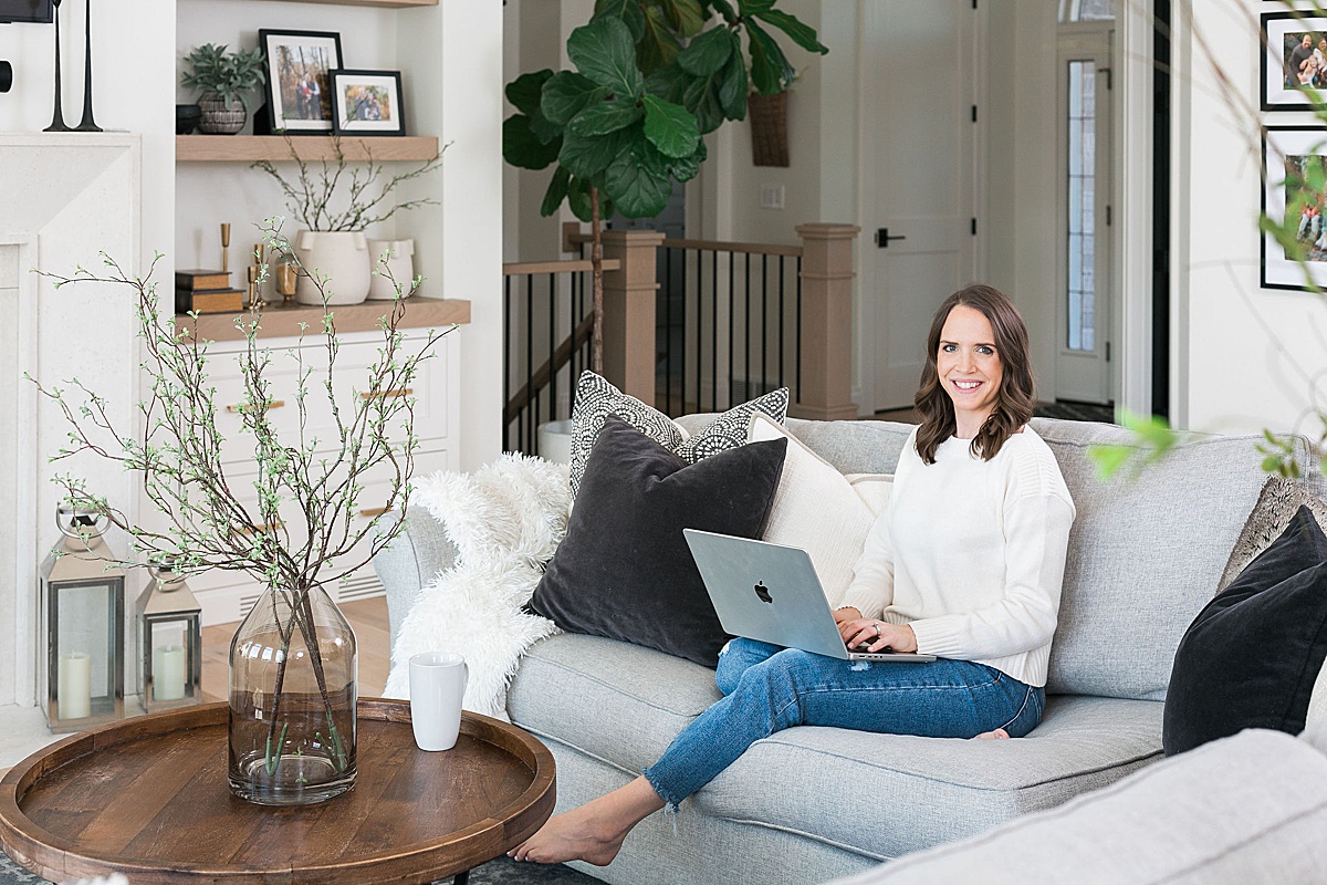 woman working on a macbook laptop on couch wearing neutral sweater and denim jeans