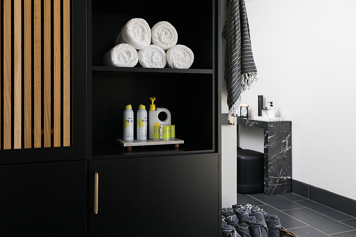 pool house bathroom with black and white color theme, goop products and towel shelf